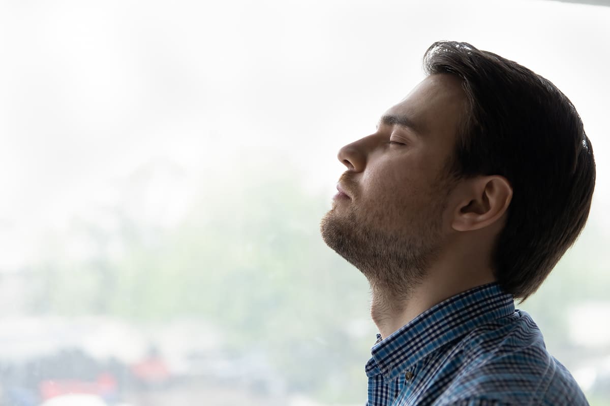 Man with eyes closed near window appearing relaxed, representing post-session calm and mental clarity from Braintap therapy.