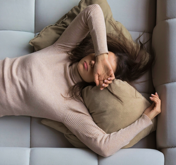 Tired woman lying on couch covering face, representing symptoms like fatigue and poor sleep treatable with peptide therapy