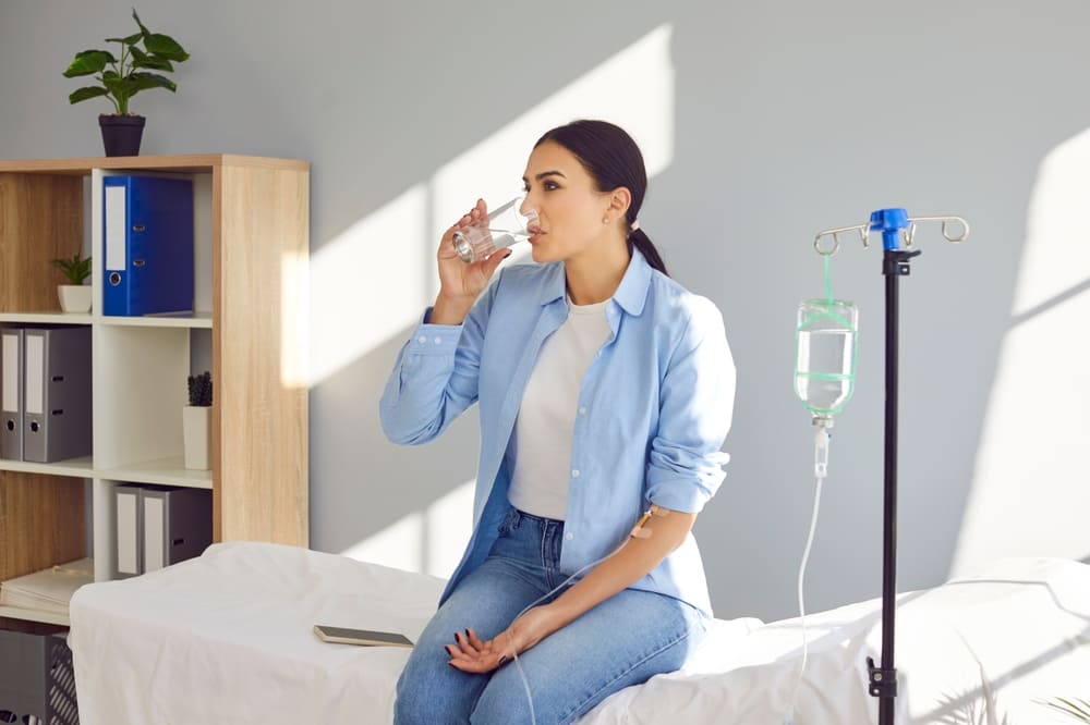 Woman drinking water during IV therapy session, representing hydration, relaxation, and supportive care for anxiety symptoms