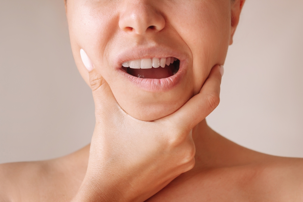 Close-up of woman touching jaw illustrating off-label Botox uses like jaw pain, facial asymmetry, and muscle tension