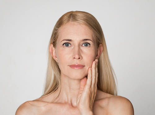 Woman in her 40s touching her cheek, illustrating XERF treatment for jawline, lower-face, and neck laxity.
