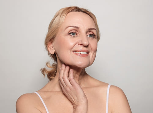 Smiling woman touching her neck, illustrating XERF guidance for slower collagen response and skin laxity after 50.